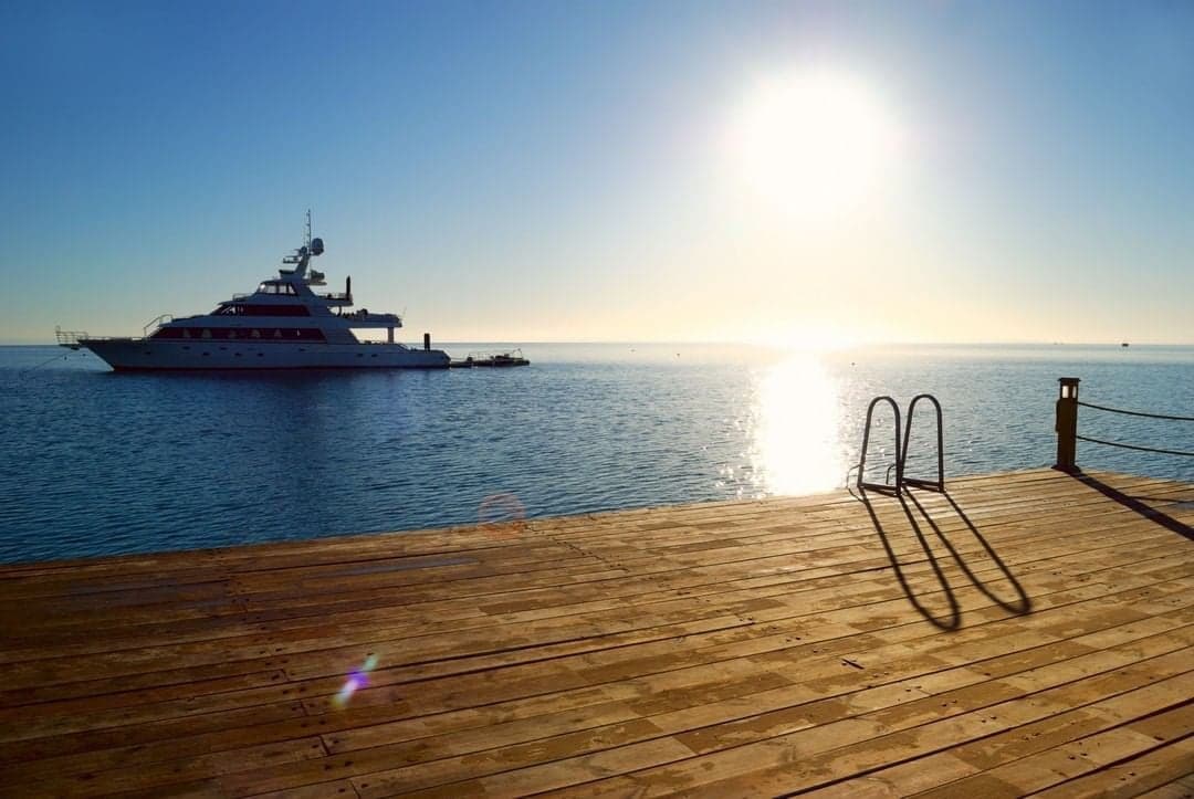 A superyacht at anchor at sunrise, seen from a wooden jetty